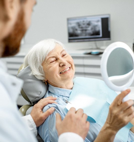 An elderly woman admiring her new dental implants in a hand mirror