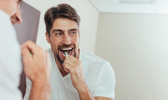 A man brushing his teeth in front of a bathroom mirror