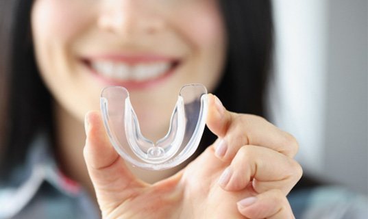 A smiling woman holding a transparent mouthguard in her hand