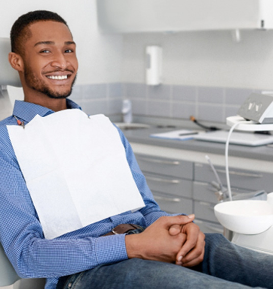 Man sitting in dental chair smiling with hands folded
