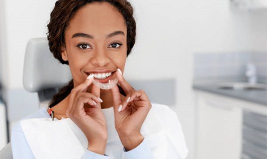 Woman in dental chair holding clear aligner