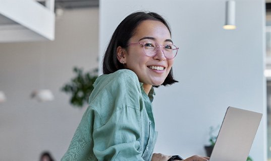 Woman with glasses smiling while working on laptop