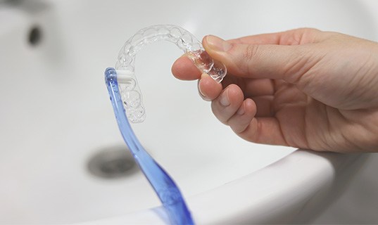 Patient using toothbrush to clean aligner