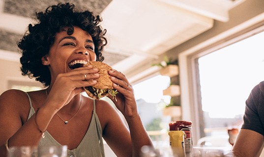 Woman smiling while eating sandwich at restaurant