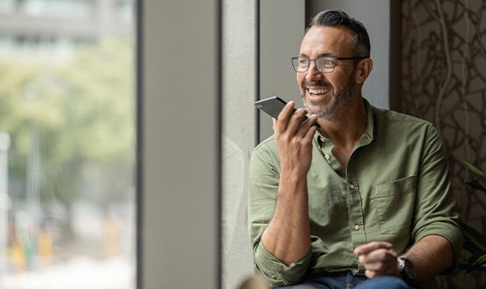 Man smiling while talking on speaker phone